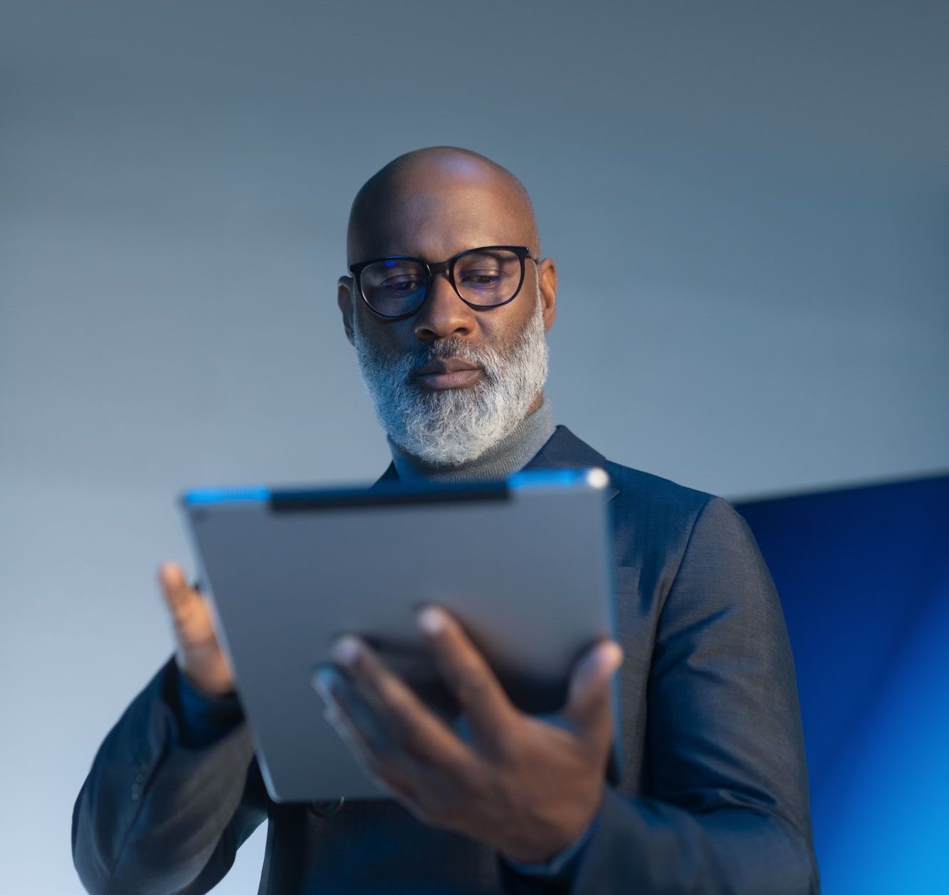 Schwarzer Mann mit Brille und grauem Bart schaut auf ein Tablet.