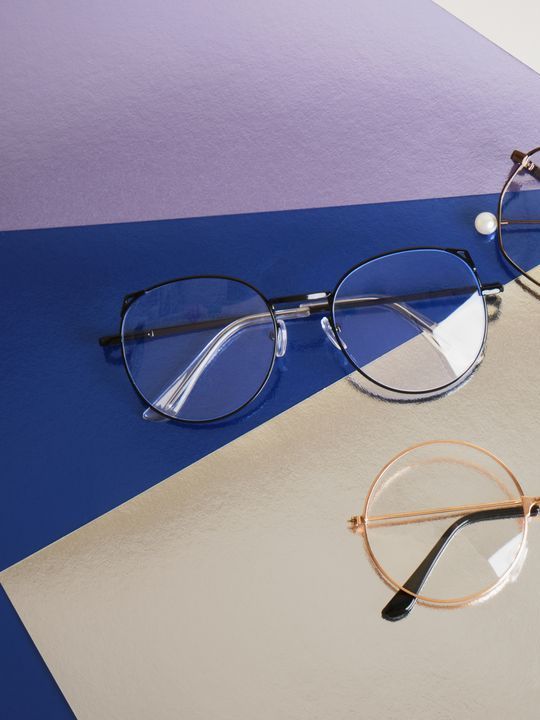Brillen mit schwarzem, goldenem und silbernem Rahmen auf blauem, violettem und beigem Hintergrund.