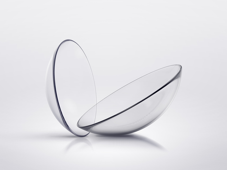 Zwei klare, gebogene Kontaktlinsen auf weißem Hintergrund.