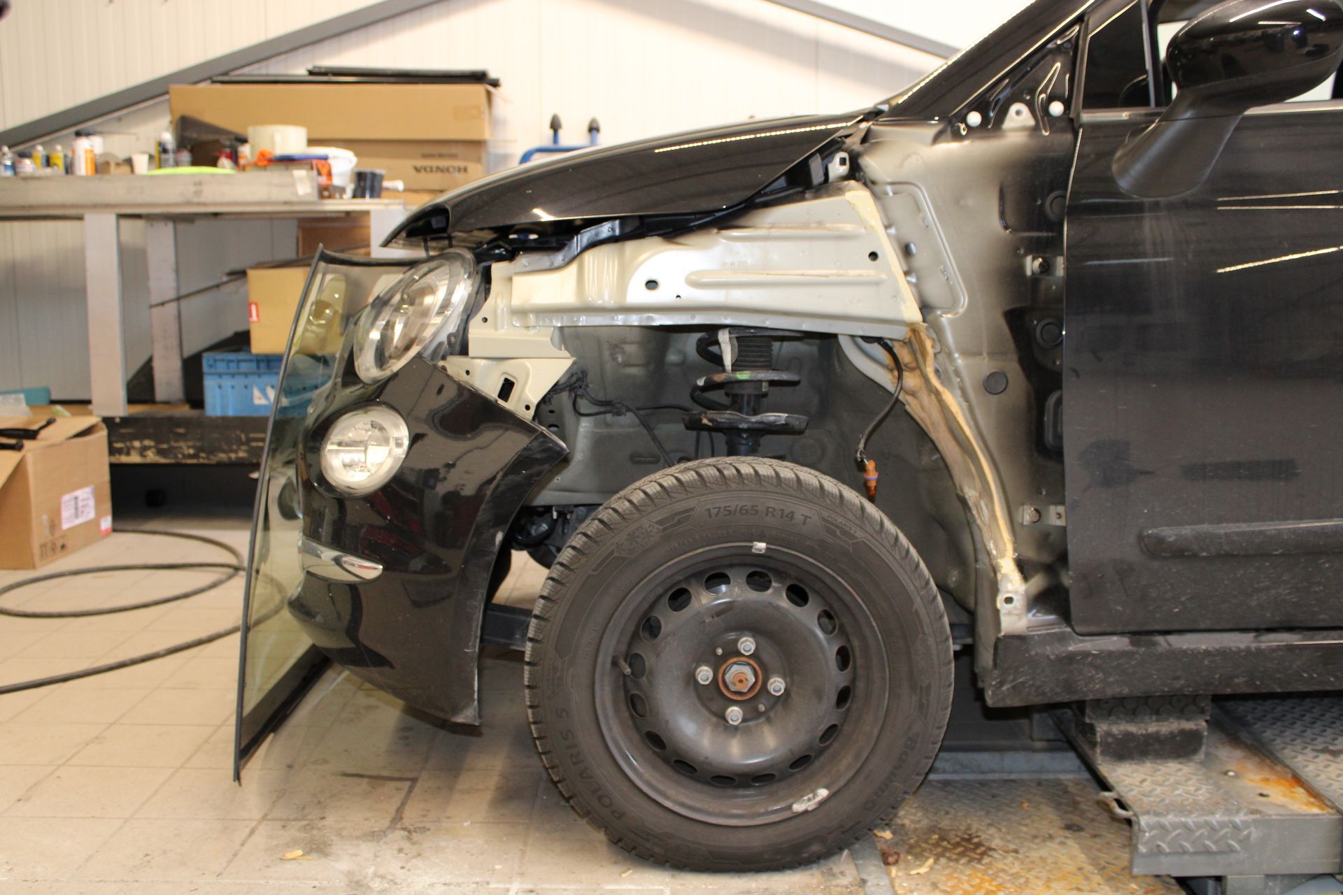Ein schwarzes Auto mit abgenommener Motorhaube steht auf einer Hebebühne in einer Garage.
