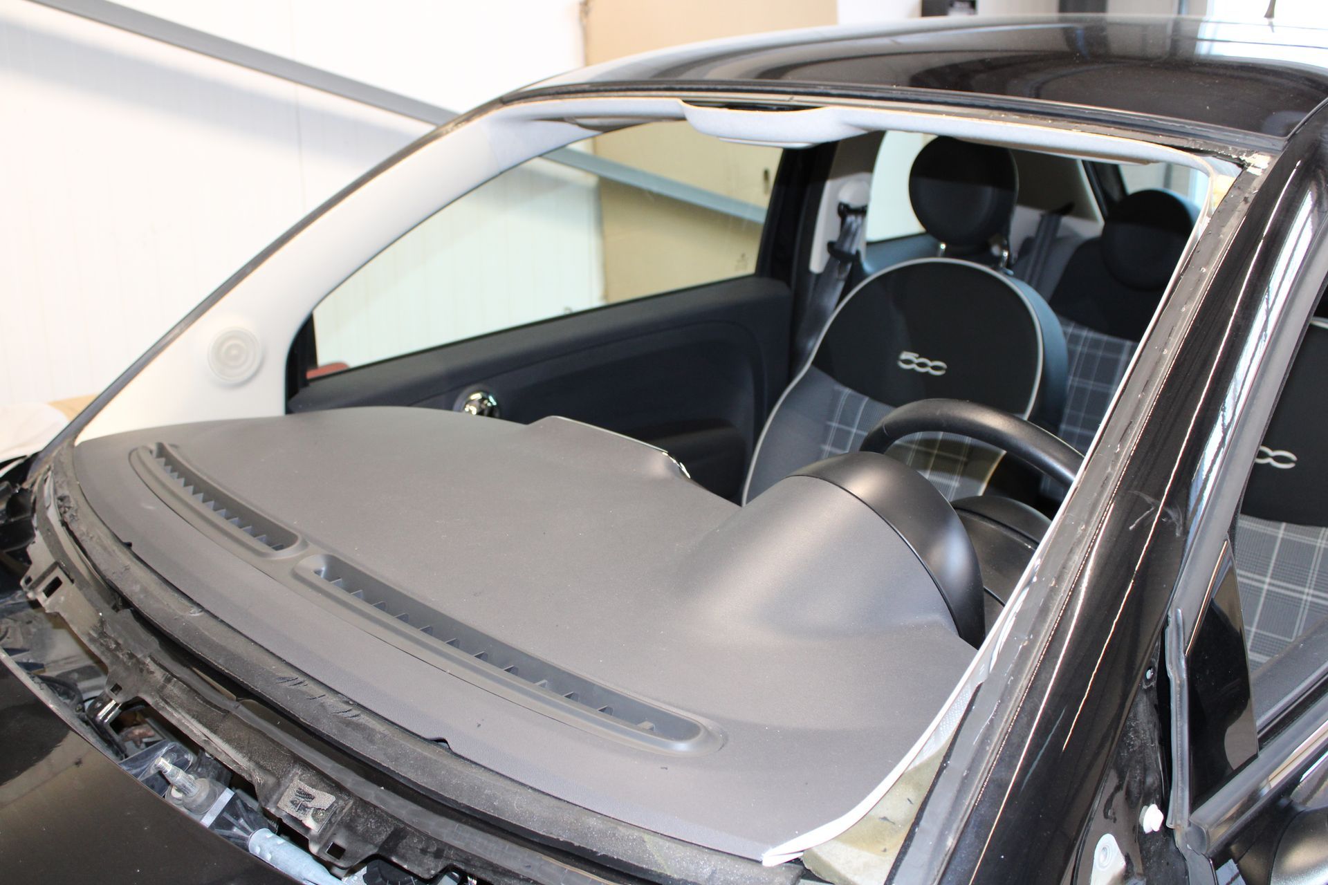 Ein schwarzes Auto mit kaputter Windschutzscheibe steht in einer Garage.