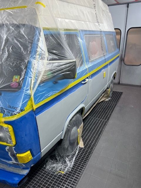 Ein blau-weißer Lieferwagen wird in einer Lackierkabine lackiert
