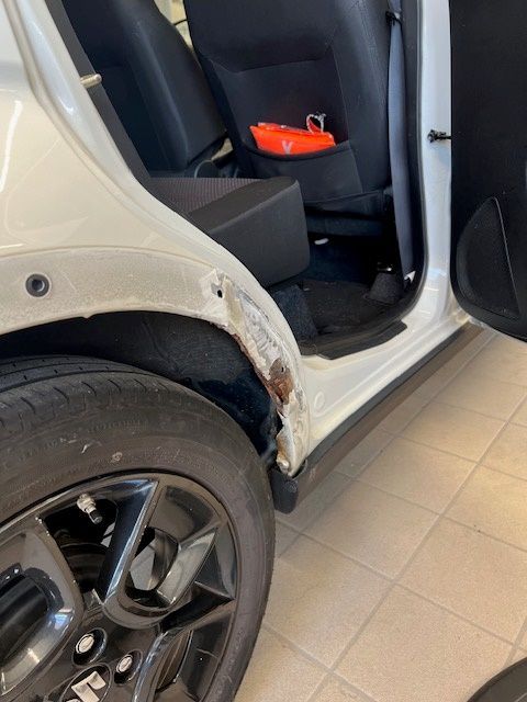Ein weißes Auto mit einem beschädigten Kotflügel in einem Ausstellungsraum