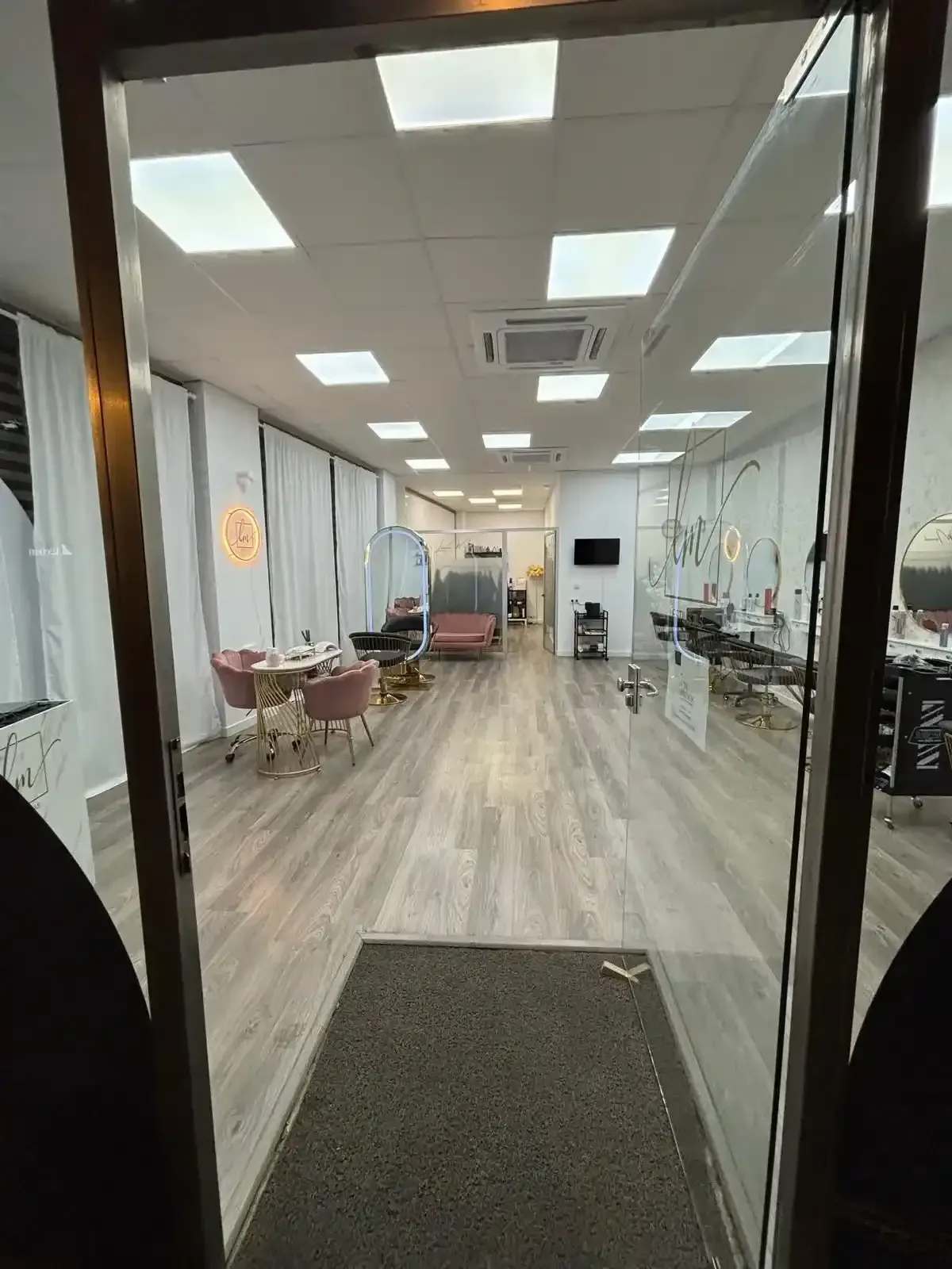 Vista a través de una puerta de una peluquería con sillas, espejos y suelos de madera clara.