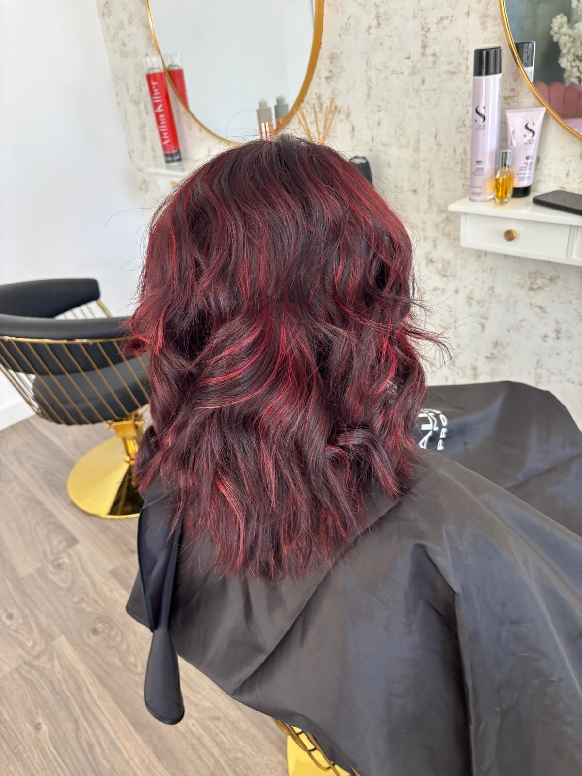 Cabello color burdeos hasta los hombros con reflejos rojos, peinado con ondas. Salón de belleza con capa negra.