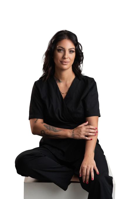 Una mujer vestida con un uniforme negro se sienta en un cubo blanco, con los brazos cruzados y mirando al espectador.