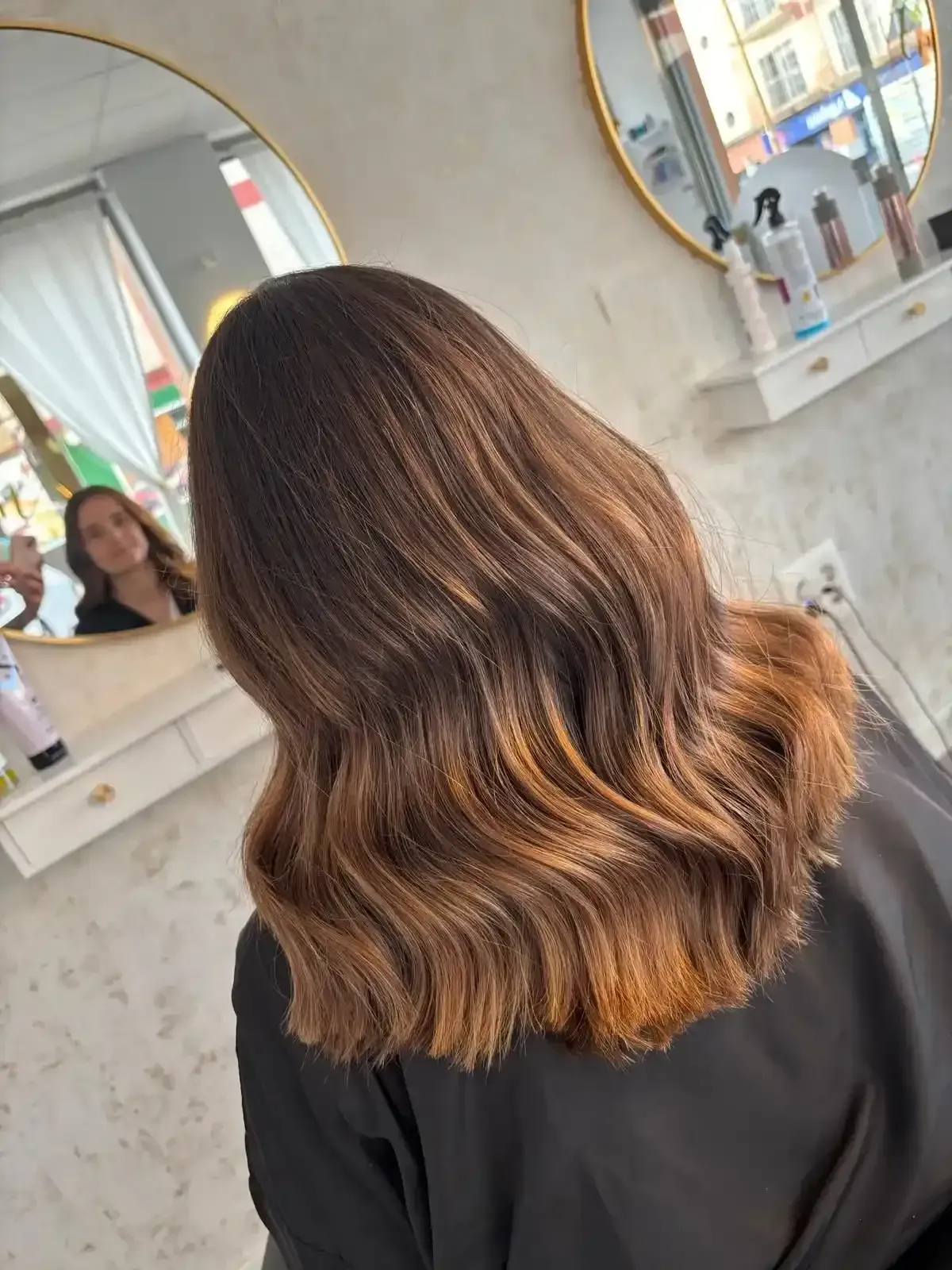 Cabello castaño de mujer con reflejos caramelo, peinado con ondas, en salón.