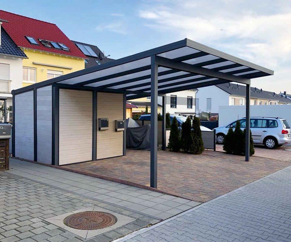 Moderner Carport aus Metall mit integriertem Abstellraum, lichtdurchlässigem Dach und gepflasterter Zufahrt in einem Wohngebiet.