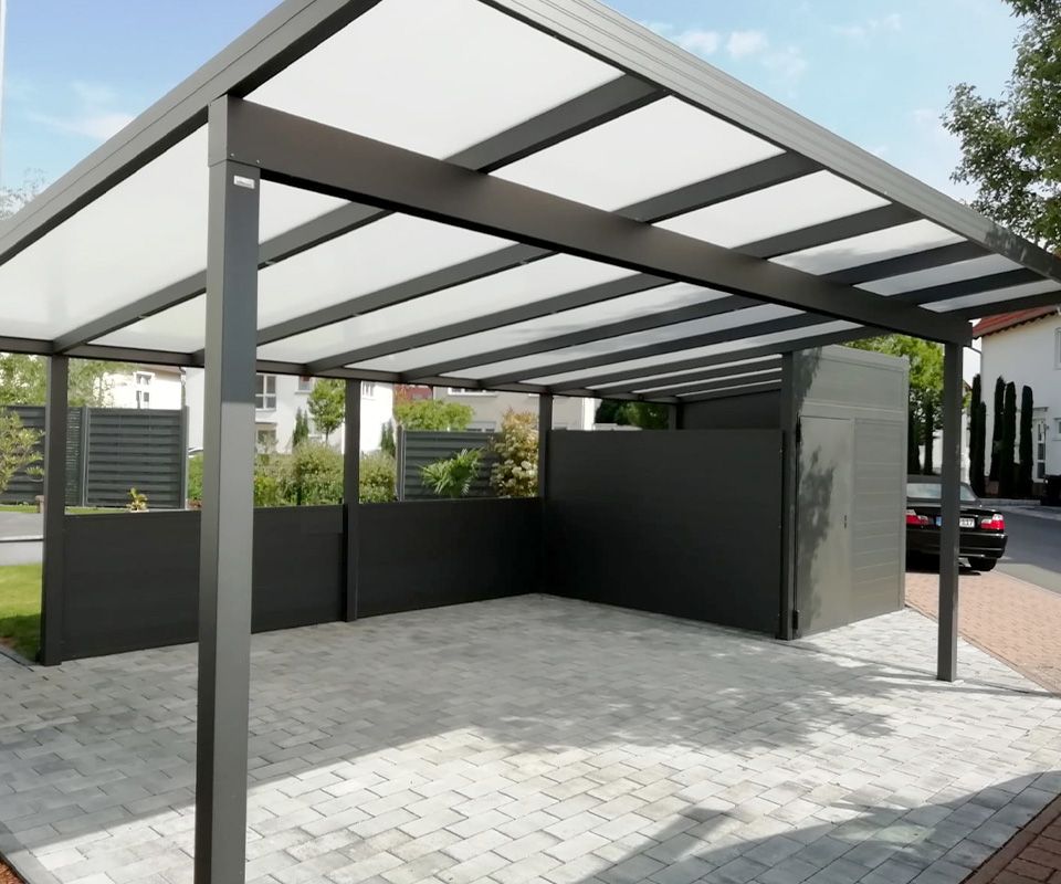 Ein moderner, dunkelgrauer Carport mit lichtdurchlässigem Dach und gepflasterter Auffahrt sowie geschlossenen Seitenwänden für mehr Privatsphäre.