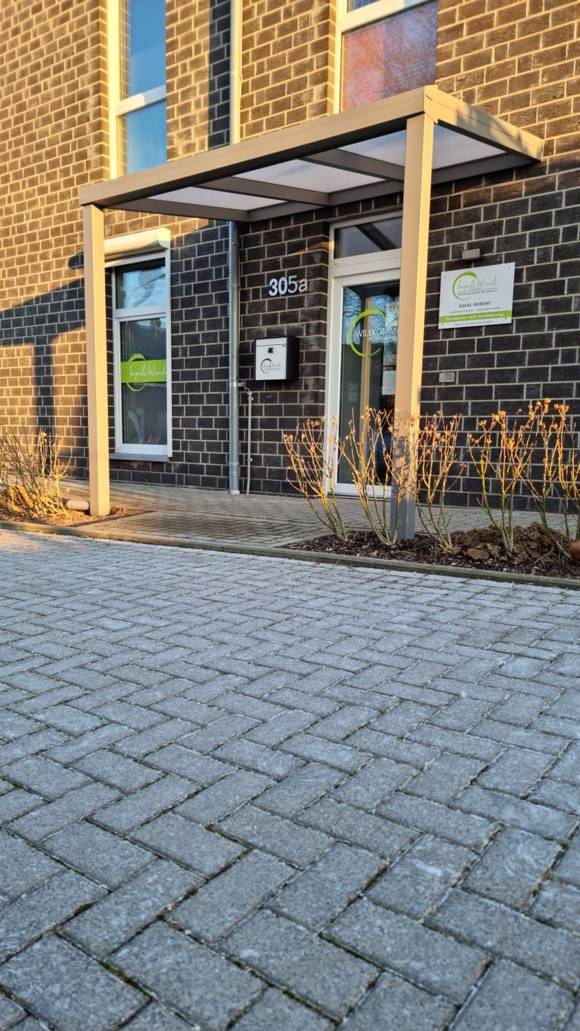 Der Außeneingang eines Backsteingebäudes mit einem modernen Metallvordach über der Glastür und einem angrenzenden Fenster.