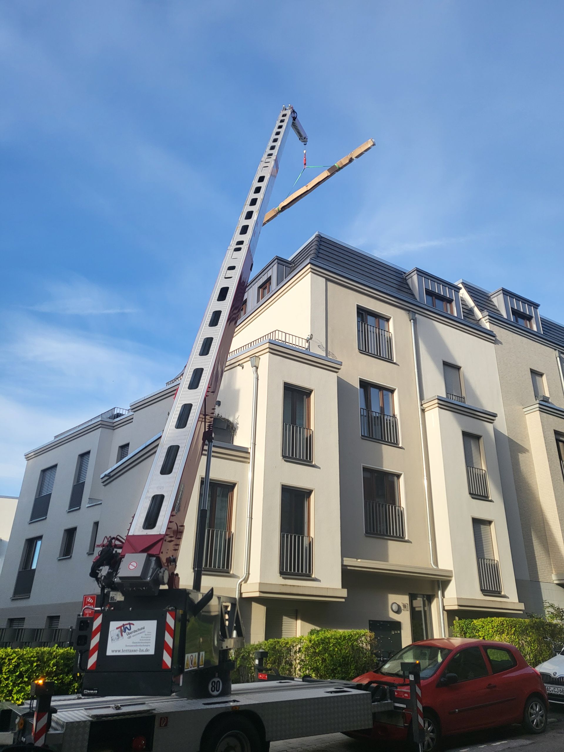 Vor einem Gebäude parkt ein Lastwagen mit einem Kran darauf.