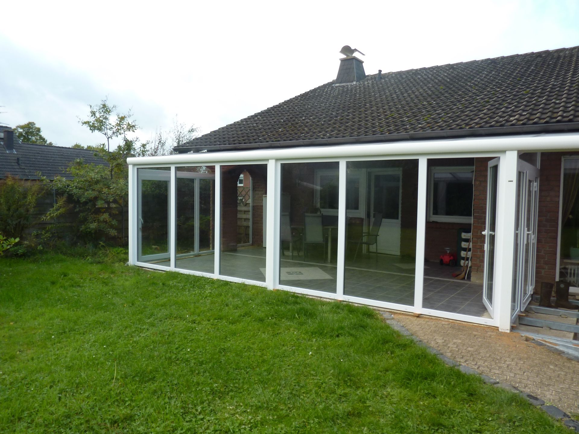 Ein weißer Glaswintergartenanbau an der Rückseite eines Backsteinhauses mit Blick auf einen grünen Rasen.