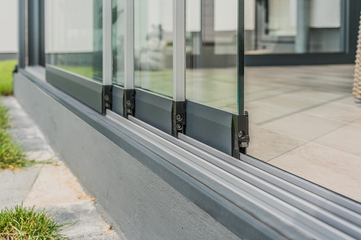 Nahaufnahme eines auf einer Terrasse installierten Glasschiebetürsystems mit grauem Metallrahmen und mehreren Glasscheiben.