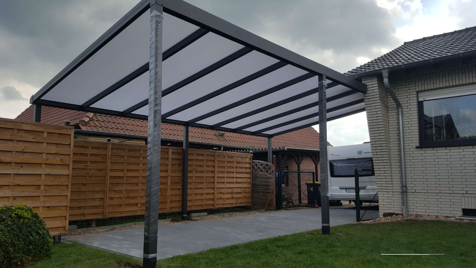 Carport mit einem transparenten Dach vor einem Backsteinhaus 