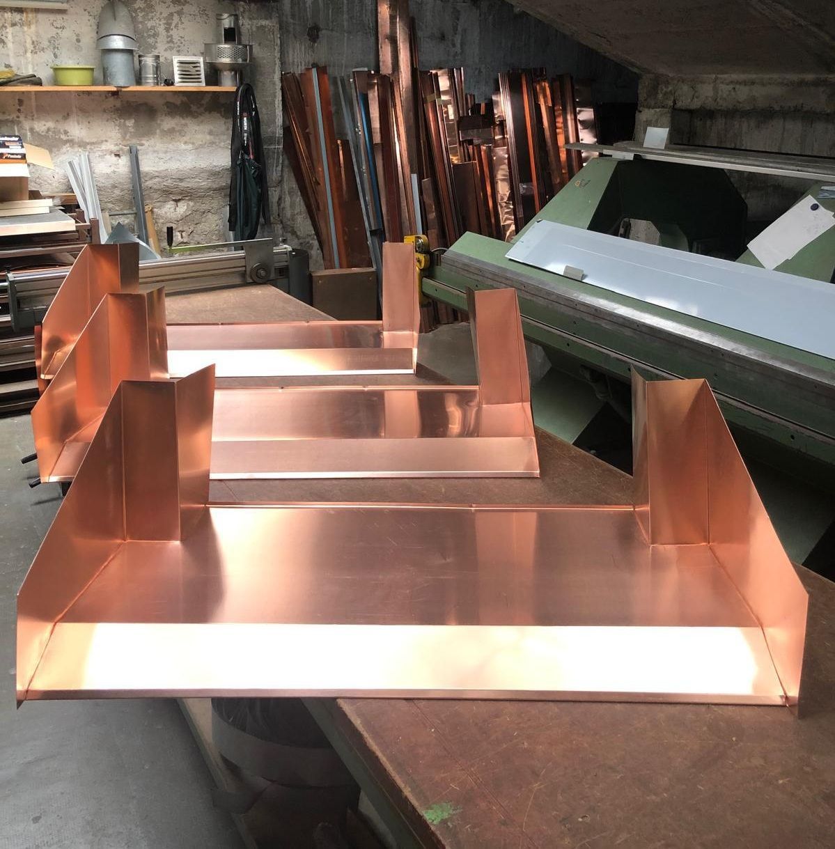 Des éléments de conduits métalliques couleur cuivre sur une table d'atelier, avec des tubes de cuivre empilés.
