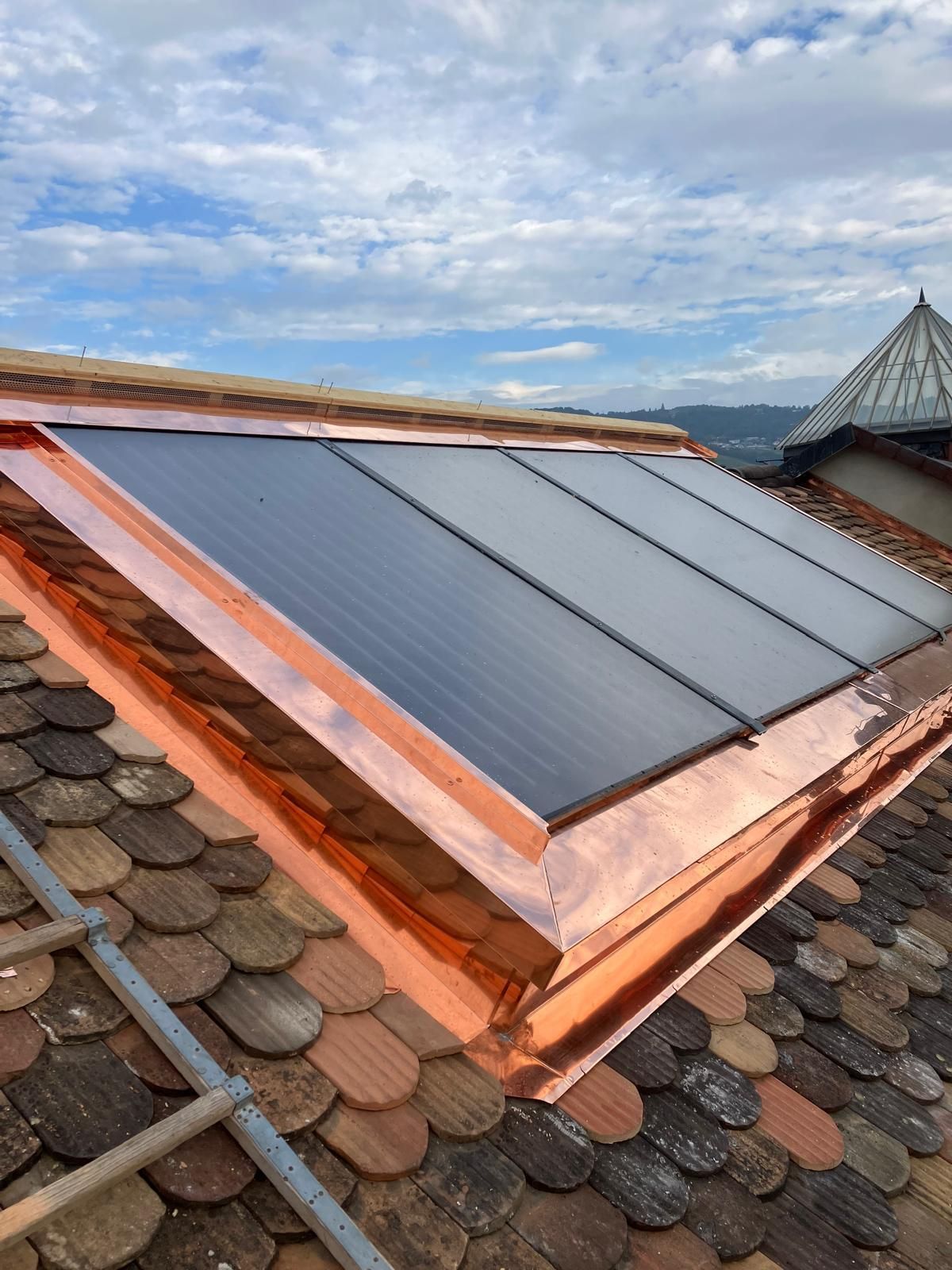 Panneaux solaires installés sur un toit en tuiles de terre cuite en pente, sous un ciel nuageux.