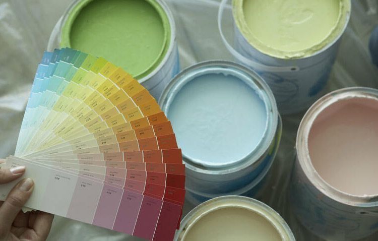 Una persona sostiene un abanico delante de un montón de latas de pintura.