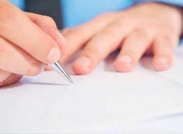 Mano de una persona sosteniendo un bolígrafo, escribiendo sobre papel blanco.