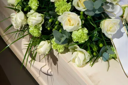 Weiße Rosen und grüne Blumen, arrangiert auf einem cremefarbenen Sarggriff