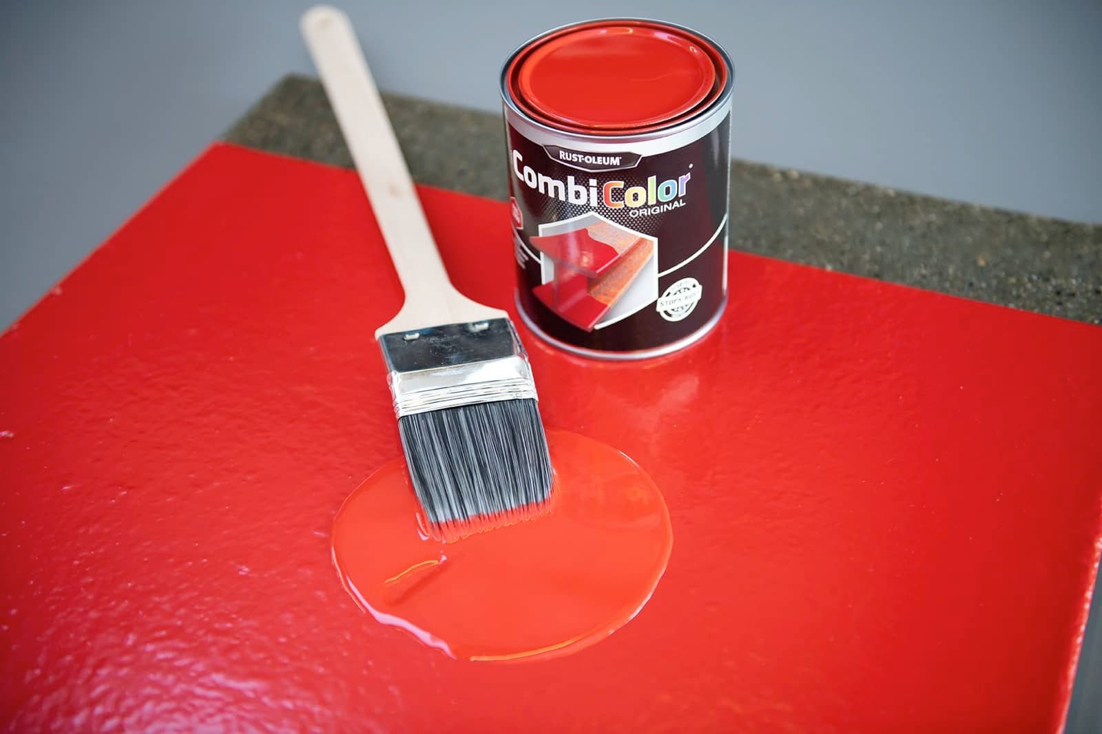 Rote Farbe, Pinsel und eine geöffnete Farbdose auf rotem Untergrund, bereit zum Malen.