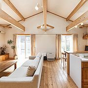 Helles, luftiges Wohnzimmer mit Holzbalken, hellem Holzboden, weissen Wänden und einem grossen weissen Sofa.