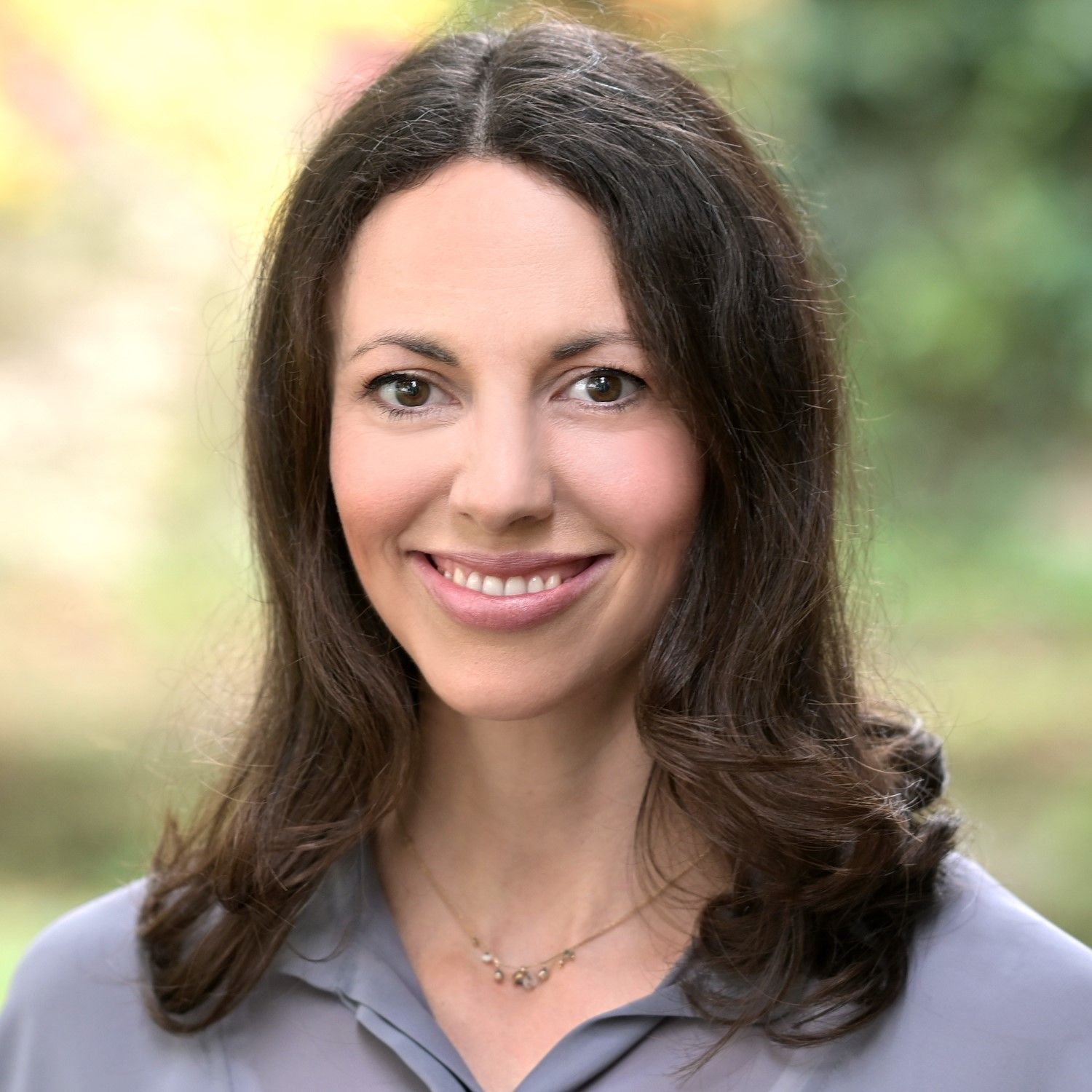 Eine Frau mit roter Brille und grünem Hemd lächelt in die Kamera.