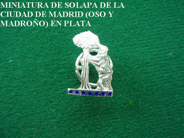 Una estatua de un oso está sobre una superficie verde con las palabras miniatura de solapa de la ciudad de madrid