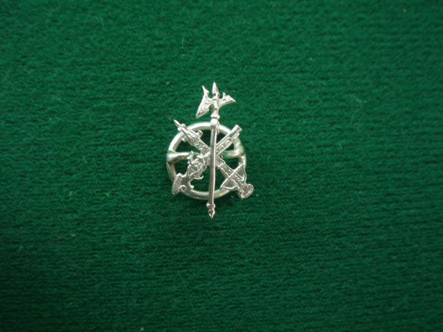 Un broche de plata con una cruz está sobre una tela verde.