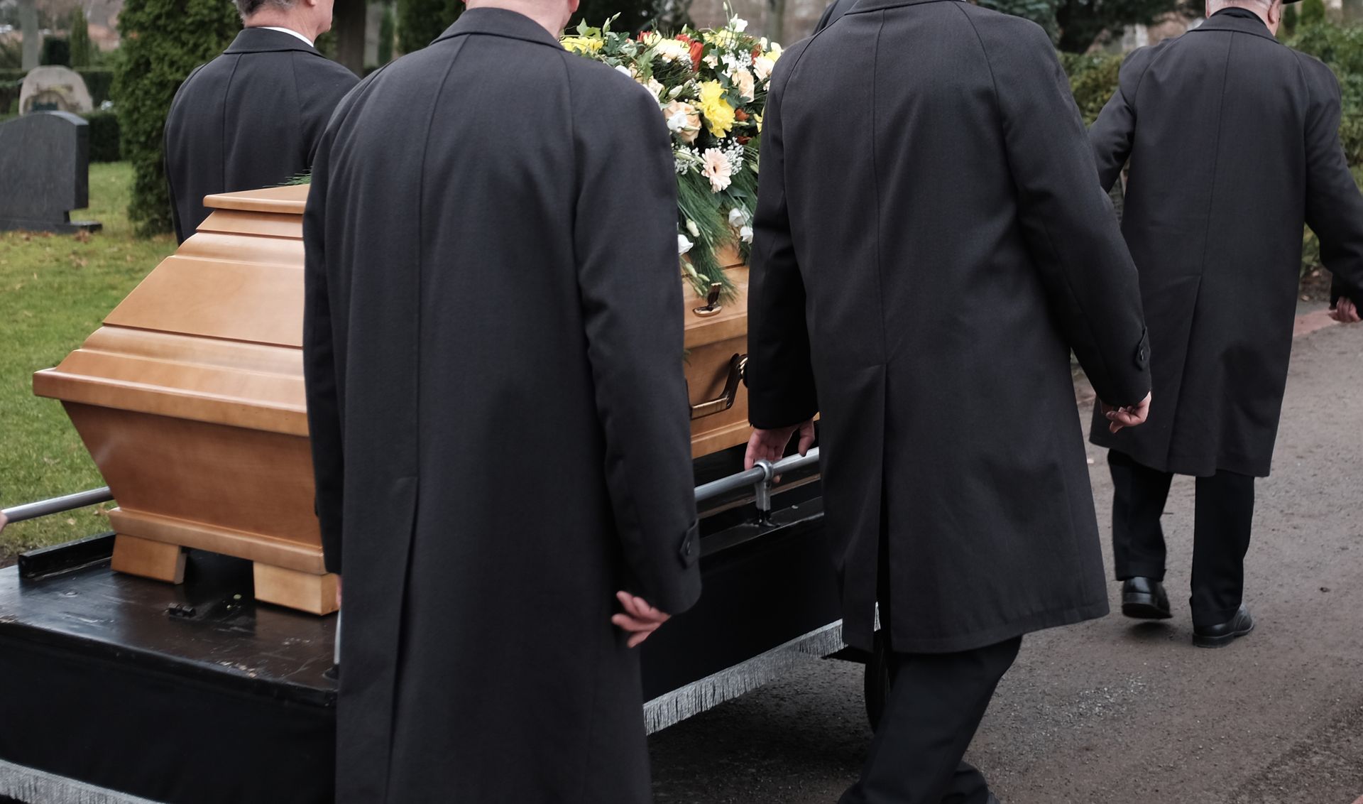 Des personnes portant un cercueil dans l'allée d'un cimetière.