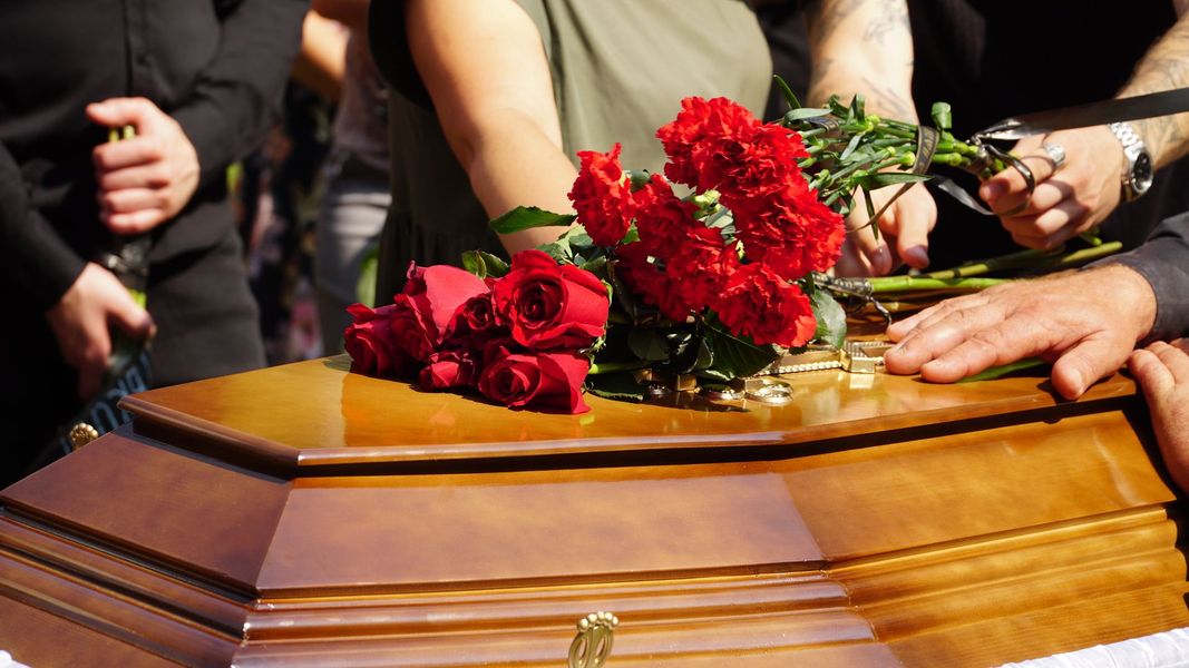 Des personnes posent des roses rouges sur un cercueil.
