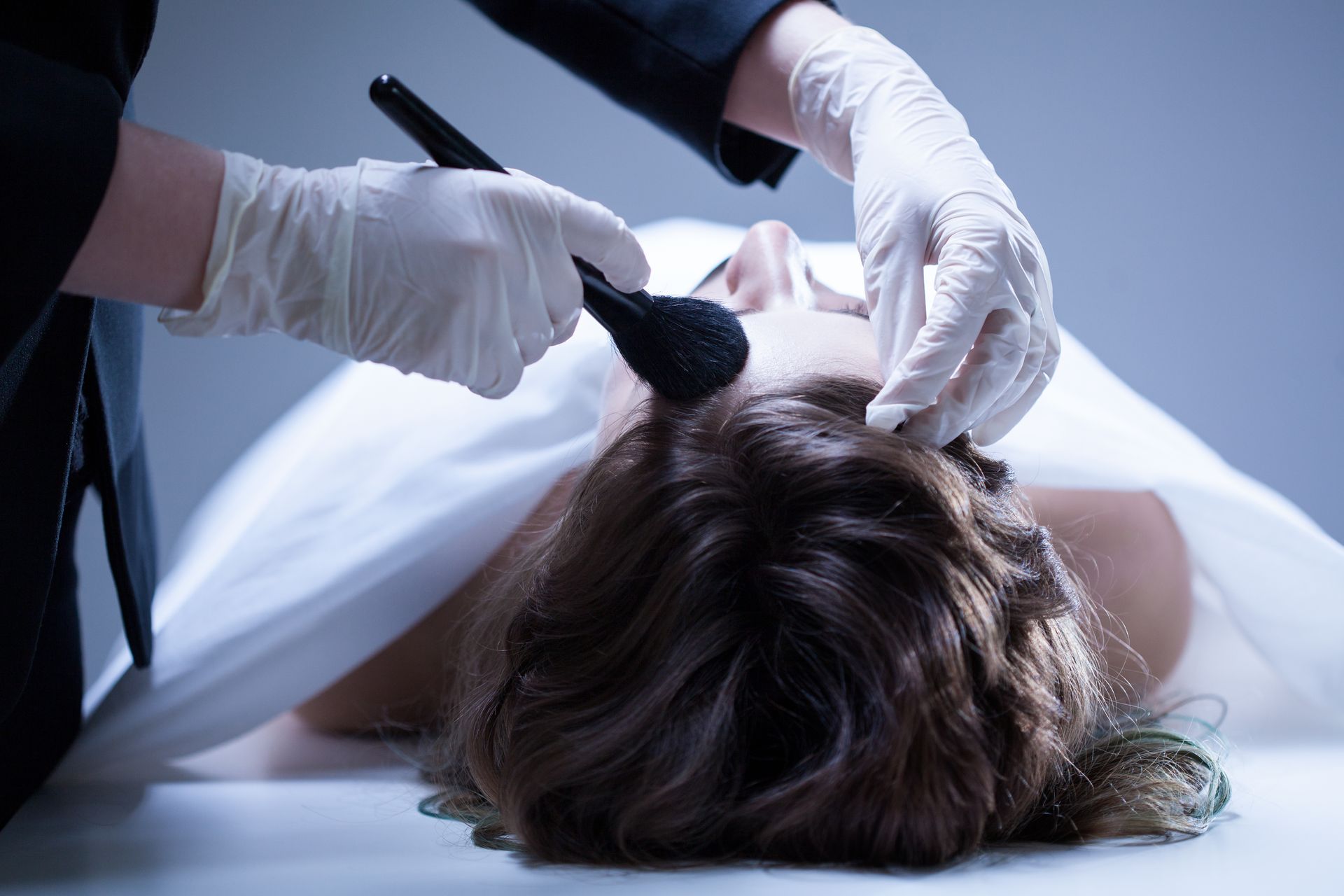Un thanatopracteur tient un pinceau de maquillage, réalisant une toilette mortuaire sur une personne décédée.