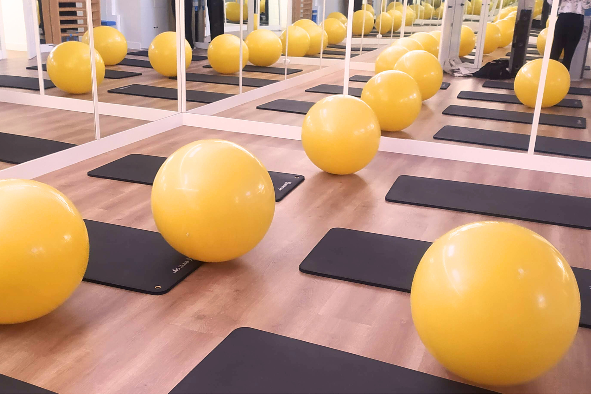 Un montón de pelotas de ejercicio amarillas están en el suelo en un gimnasio.