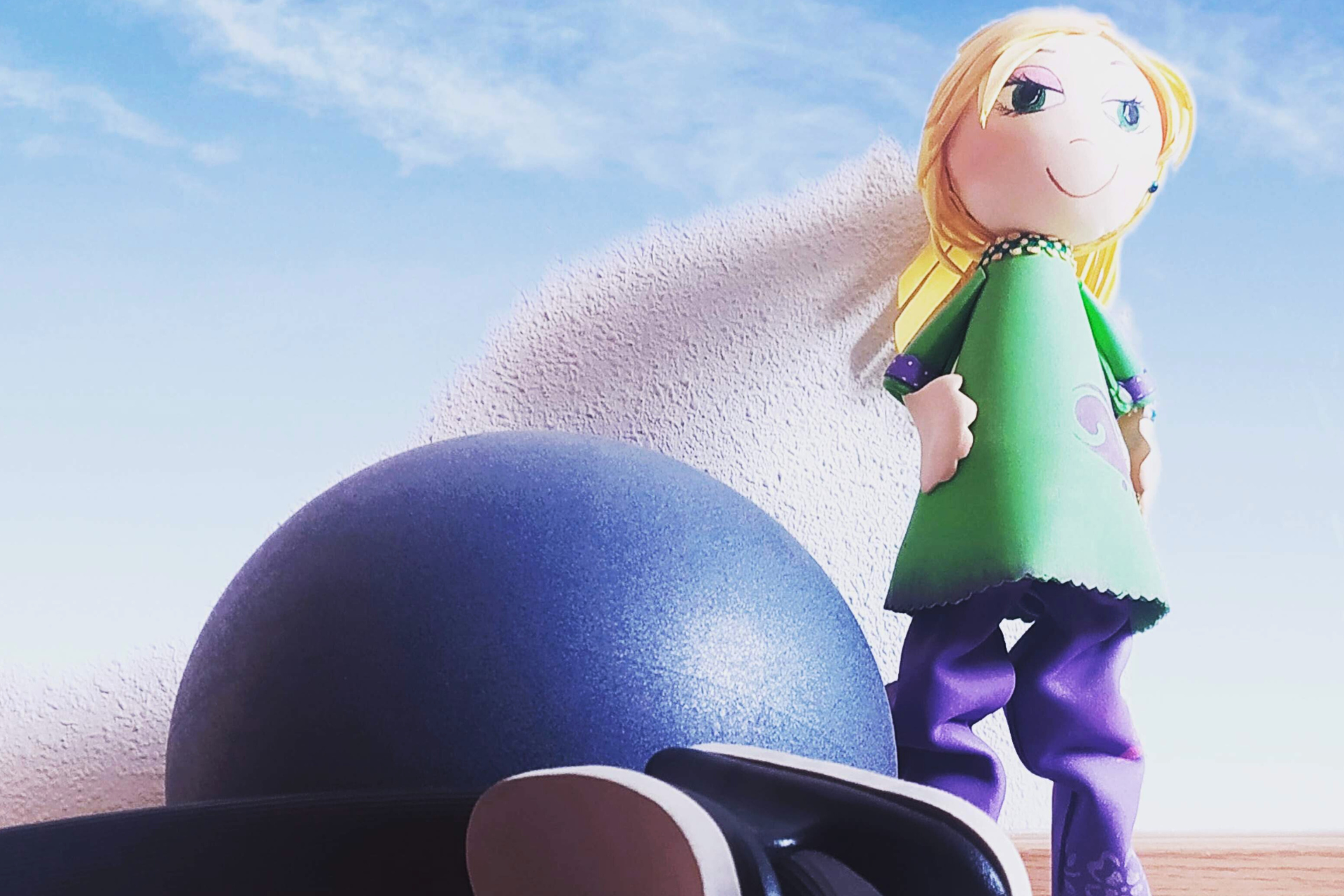 Una muñeca con un vestido verde está parada junto a una pelota azul.