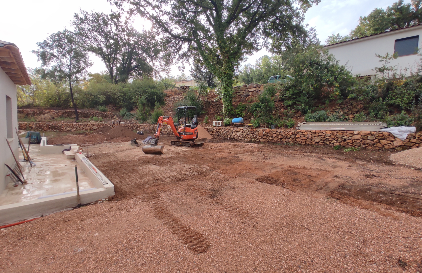 Un tracteur traverse un champ de terre devant une maison.