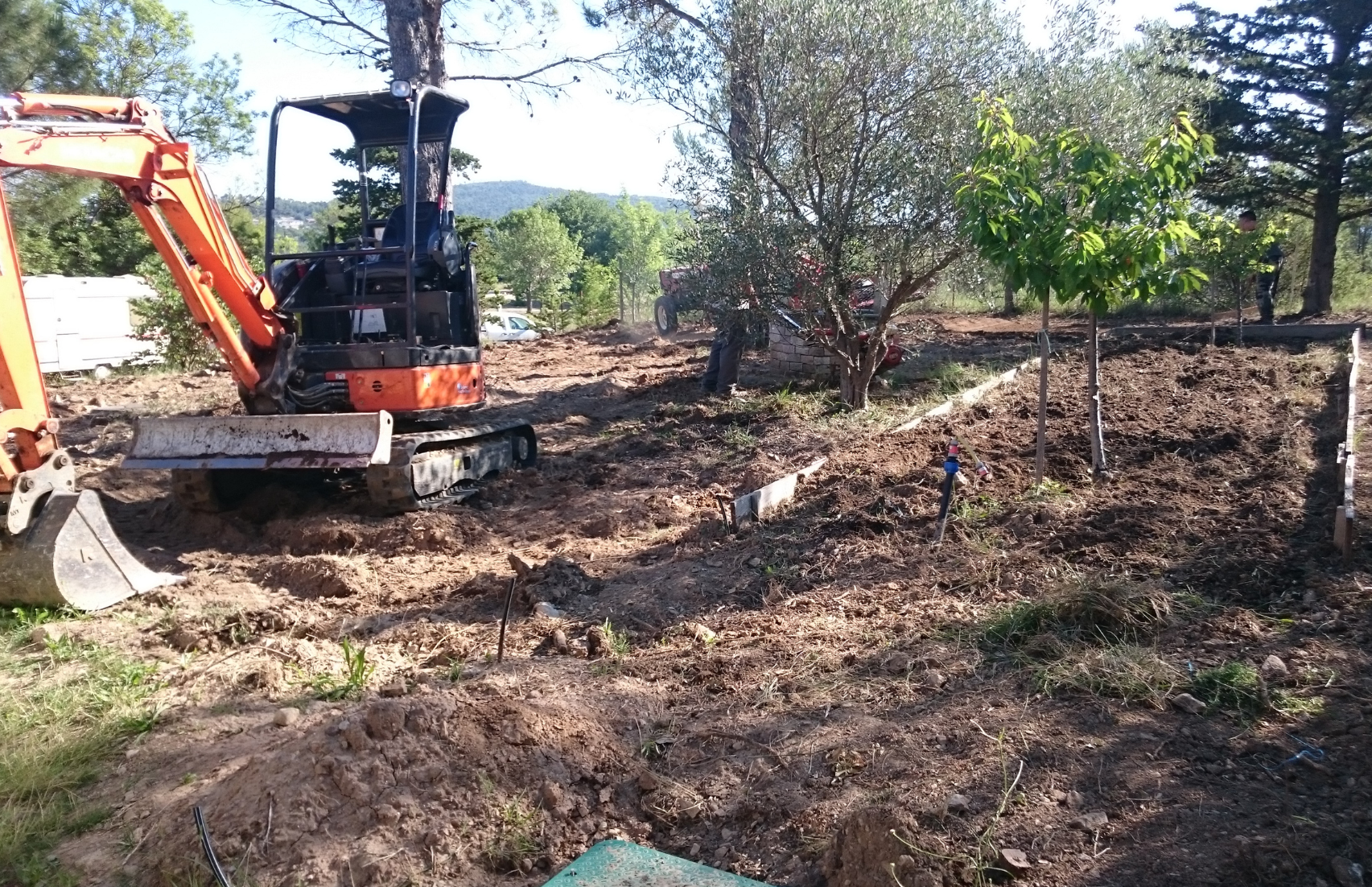 Une petite excavatrice orange creuse dans un champ de terre.