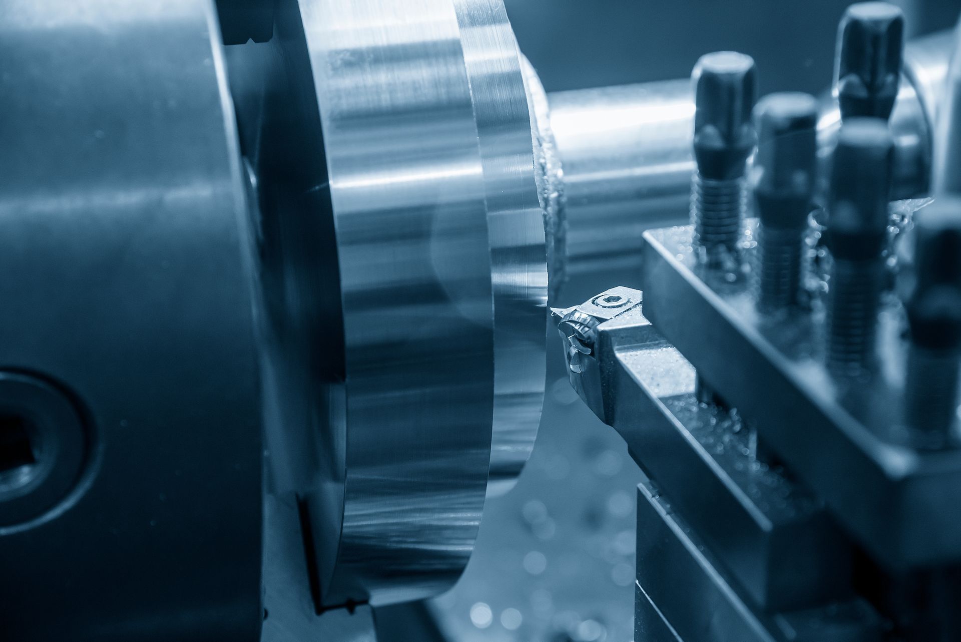 Nahaufnahme einer Metalldrehmaschine, die in einer Fabrik ein glänzendes zylindrisches Teil mit Schneidwerkzeugen bearbeitet.