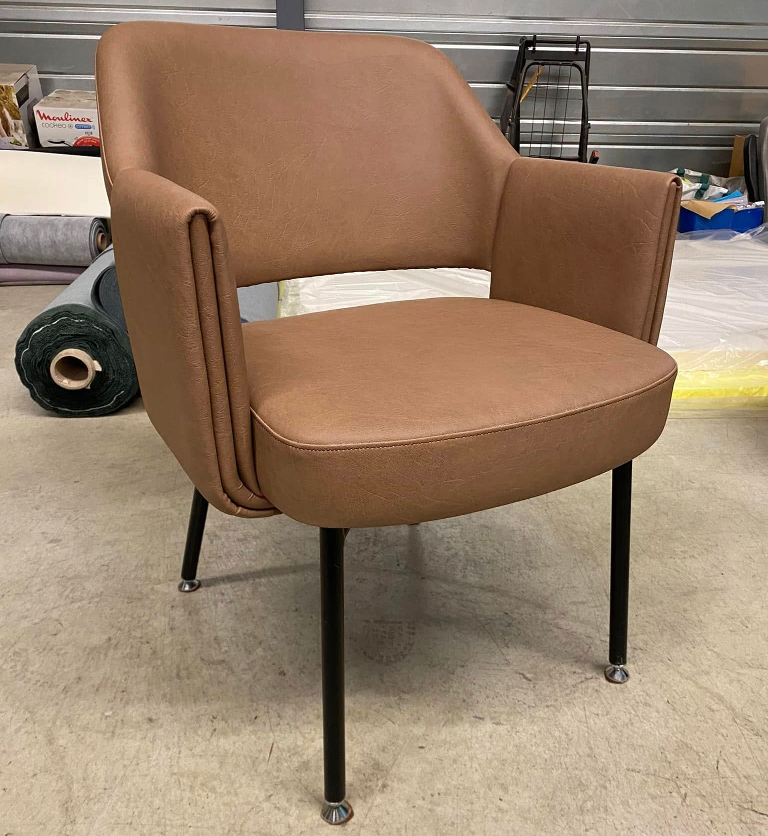 Fauteuil rembourré marron avec pieds noirs dans un atelier.