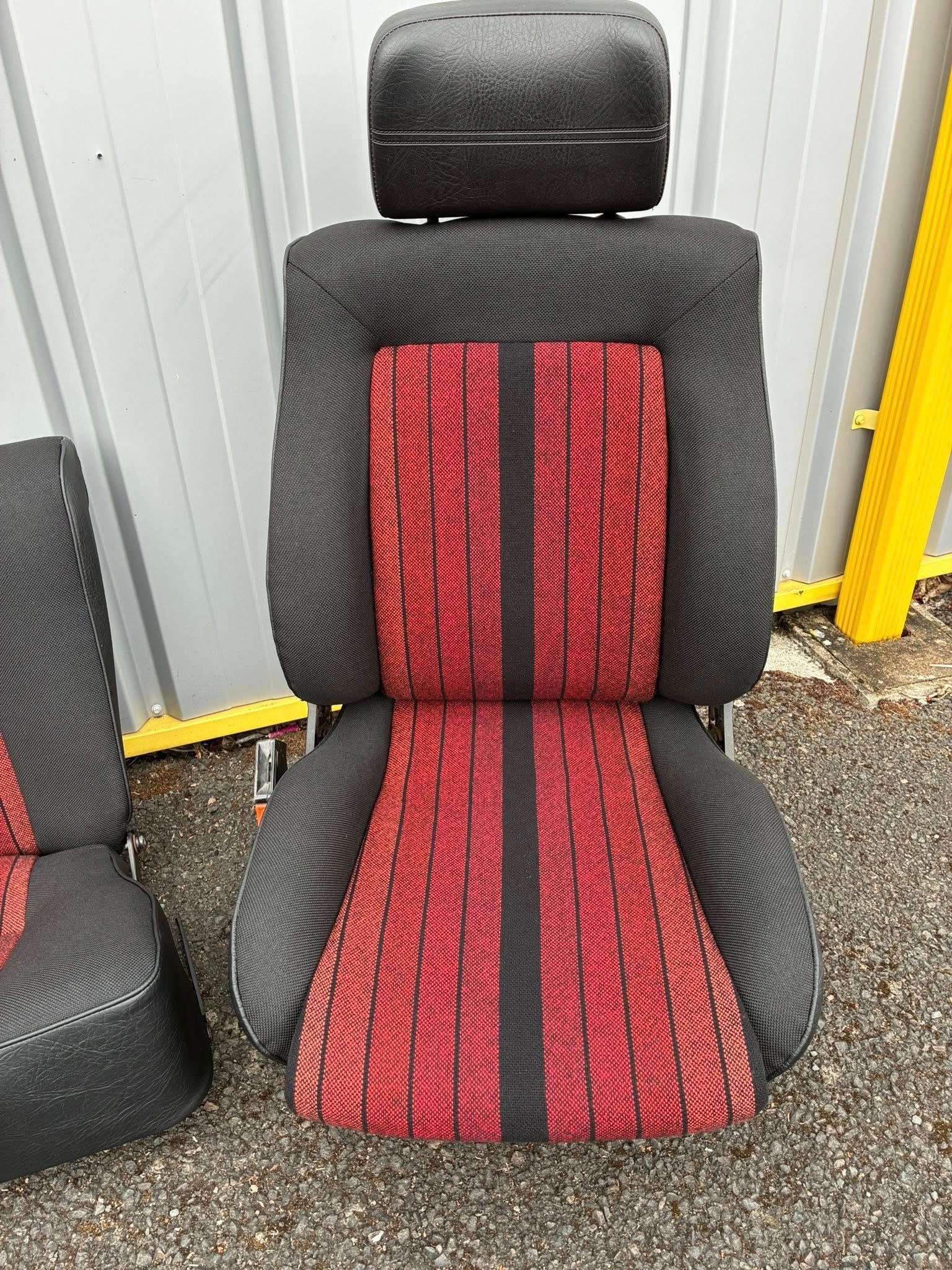 Siège auto avec revêtement en tissu noir et centre à motifs rouges. Appui-tête noir.