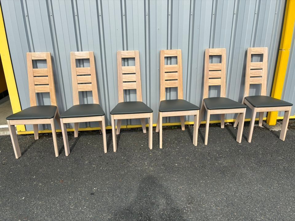 Six chaises en bois clair à assise noire sont alignées à l'extérieur, devant un fond en tôle ondulée.