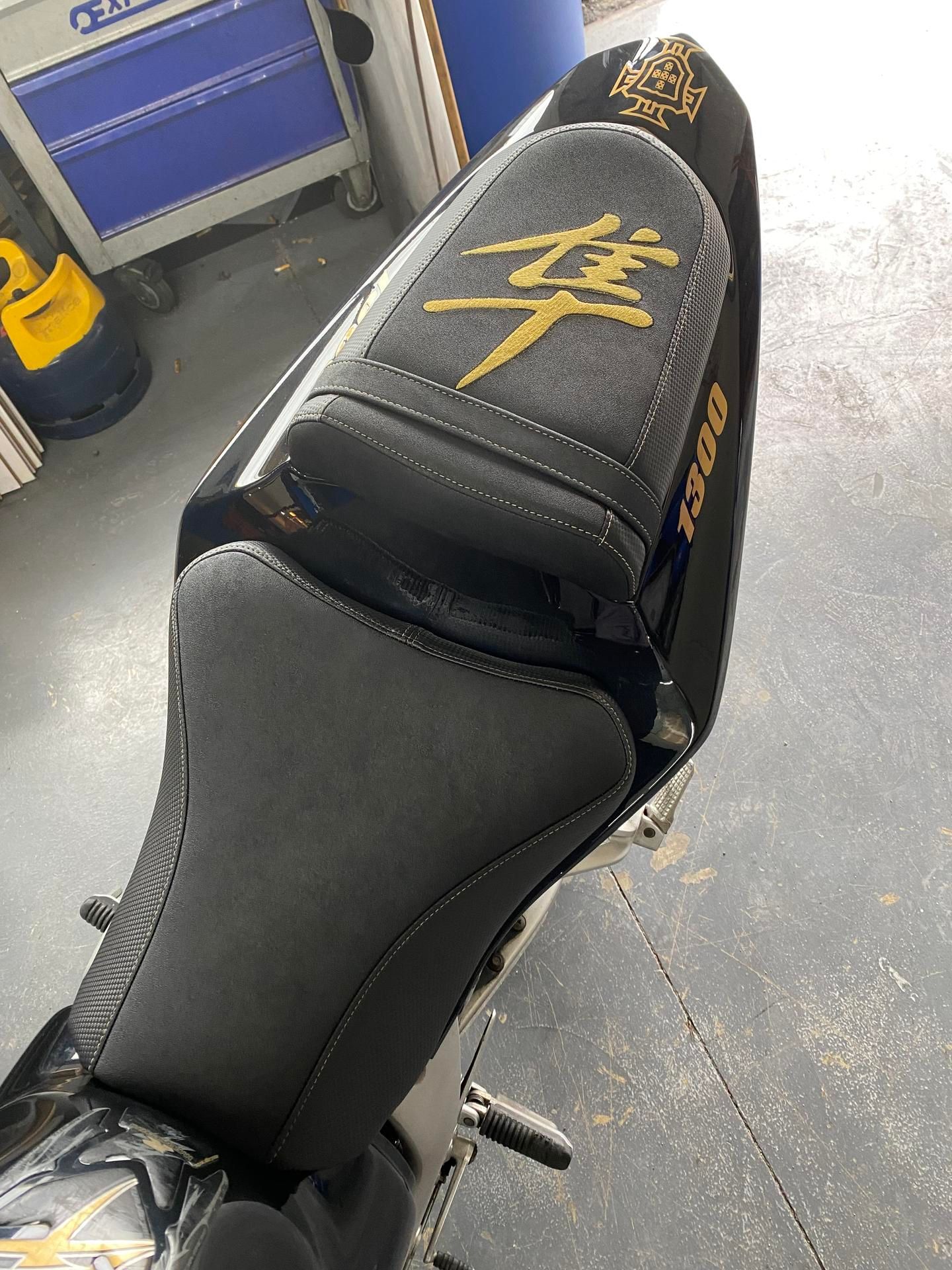Selle de moto noire avec inscriptions et surpiqûres dorées.