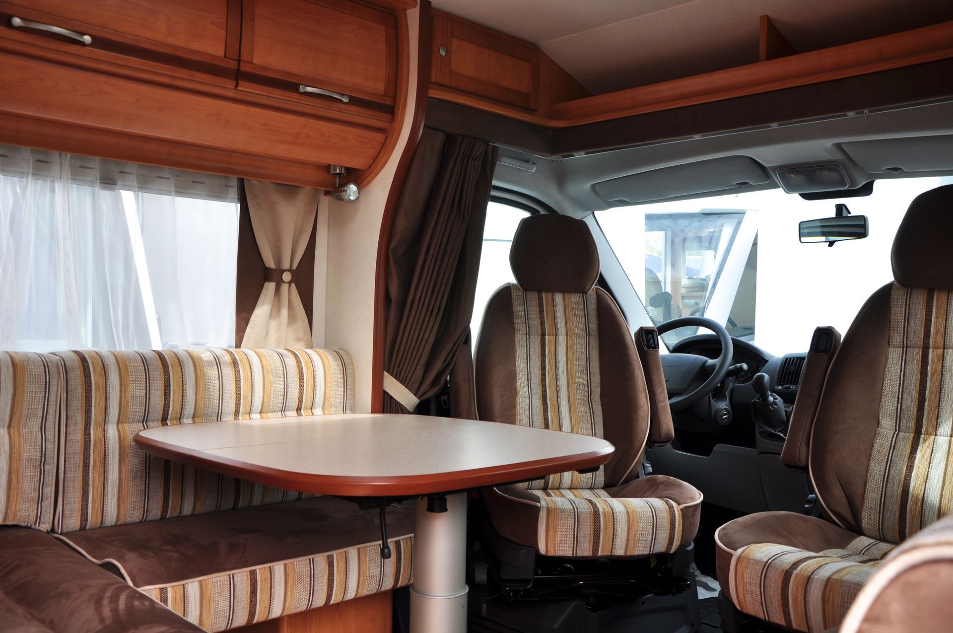 Intérieur d'un camping-car, comprenant une table, des sièges et un poste de conduite avec deux sièges, le tout dans des tons de brun et de beige.
