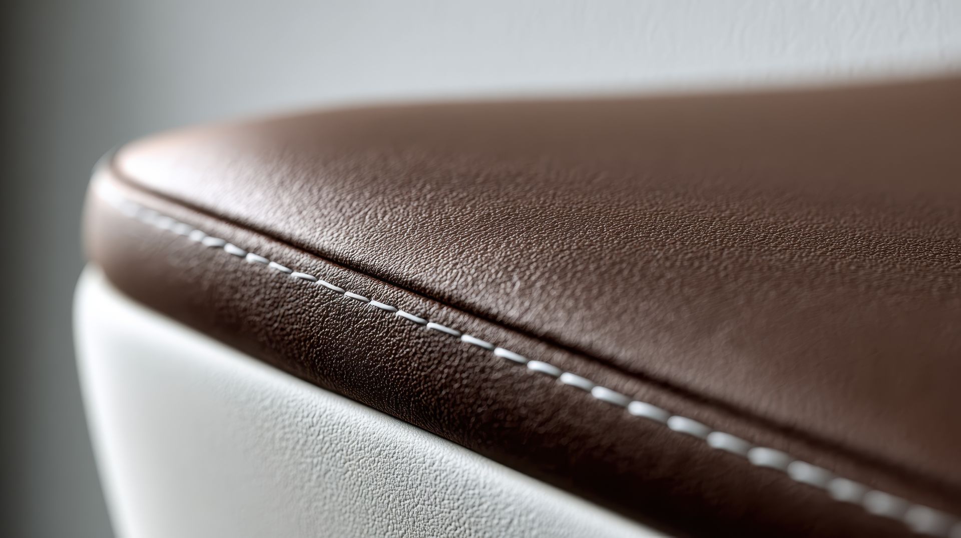 Gros plan sur un coussin en cuir marron avec des coutures blanches sur fond blanc.