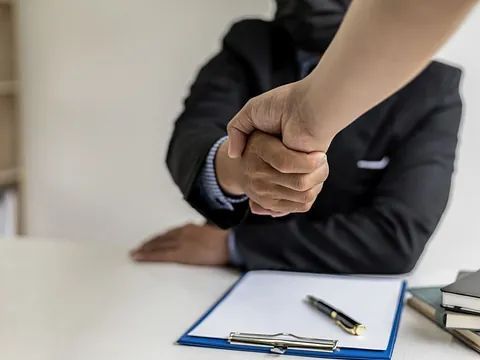 Un hombre con traje le estrecha la mano a una mujer con máscara.