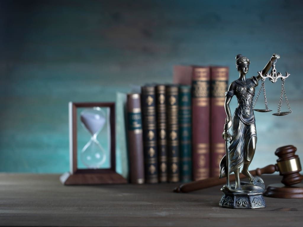 Una estatua de la justicia, un mazo y un reloj de arena están sobre una mesa de madera.
