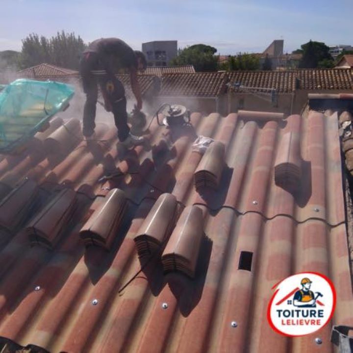 Un couvreur utilise une scie électrique sur un toit de tuiles, créant de la poussière.