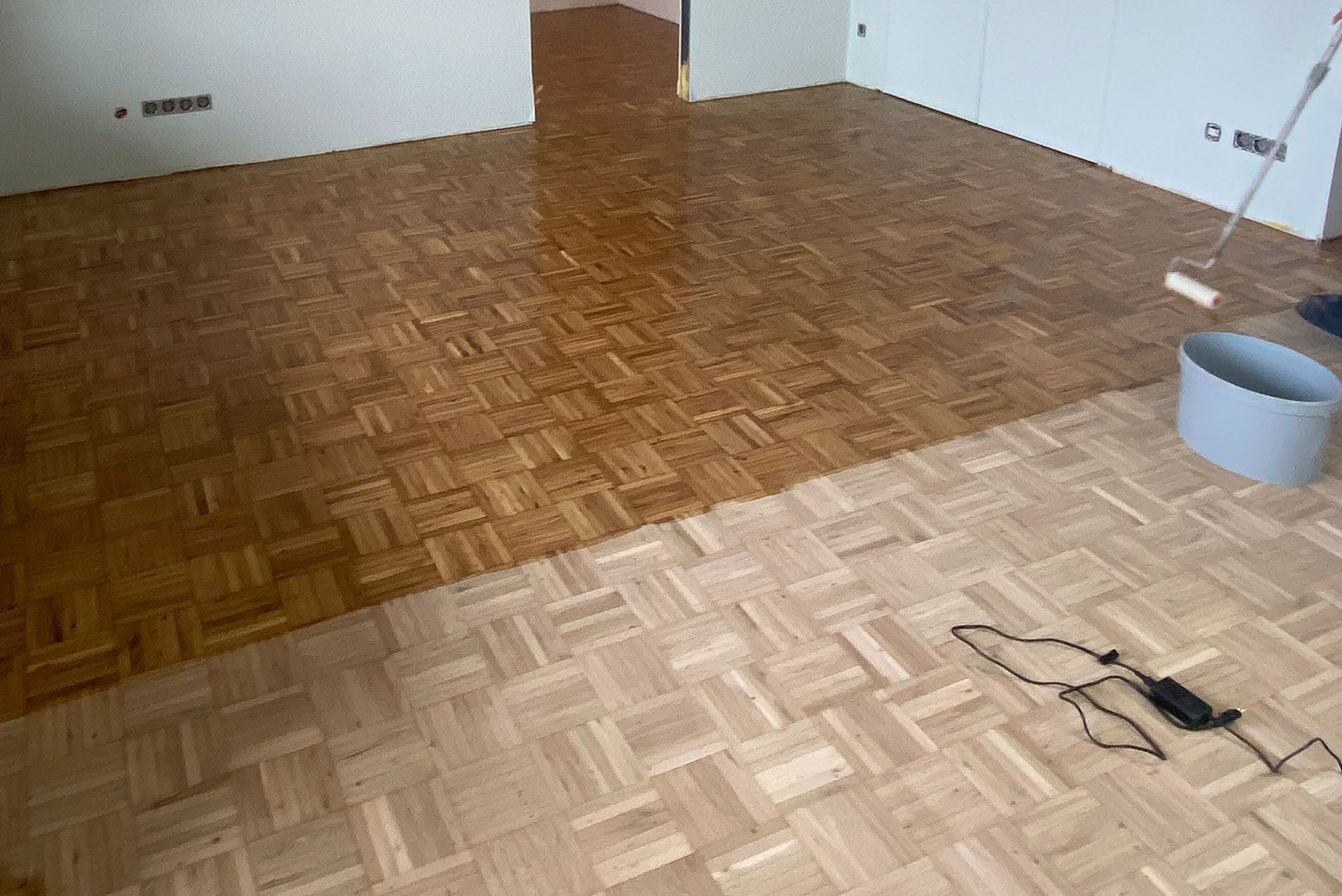 Eine Person streicht einen Holzboden mit einer Rolle.
