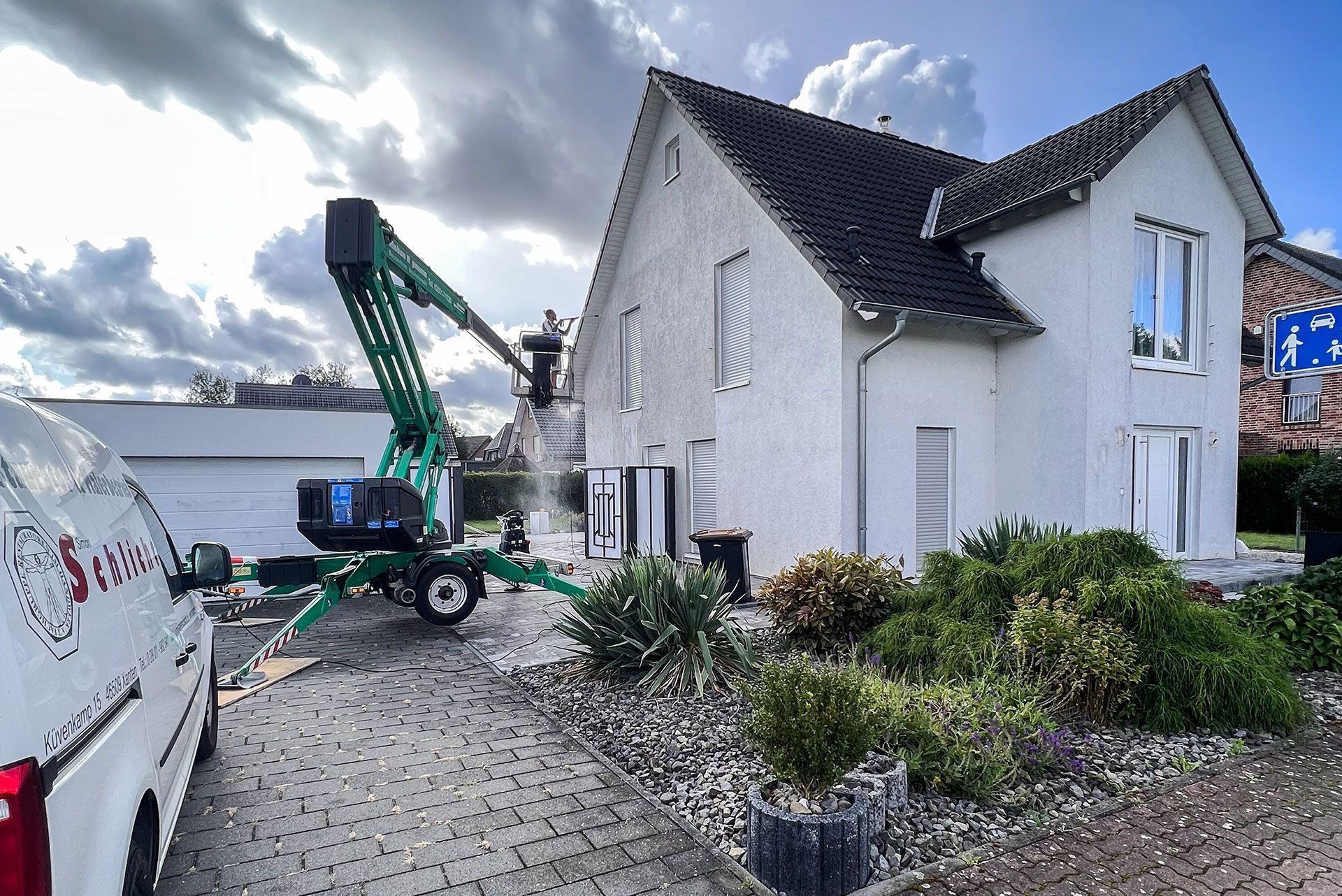 Mann auf einem Kran reinigt die Fassade eines weißen Hauses