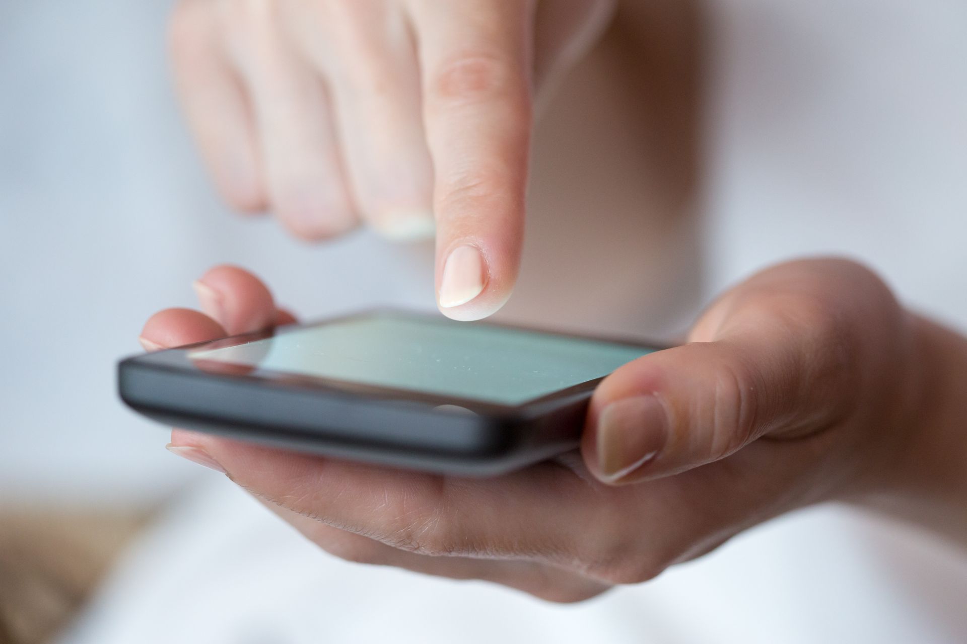 Eine Frau benutzt ein Smartphone, während ihr Finger auf dem Bildschirm liegt.