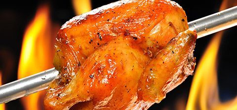 Se está cocinando un trozo de pollo en un pincho sobre el fuego.