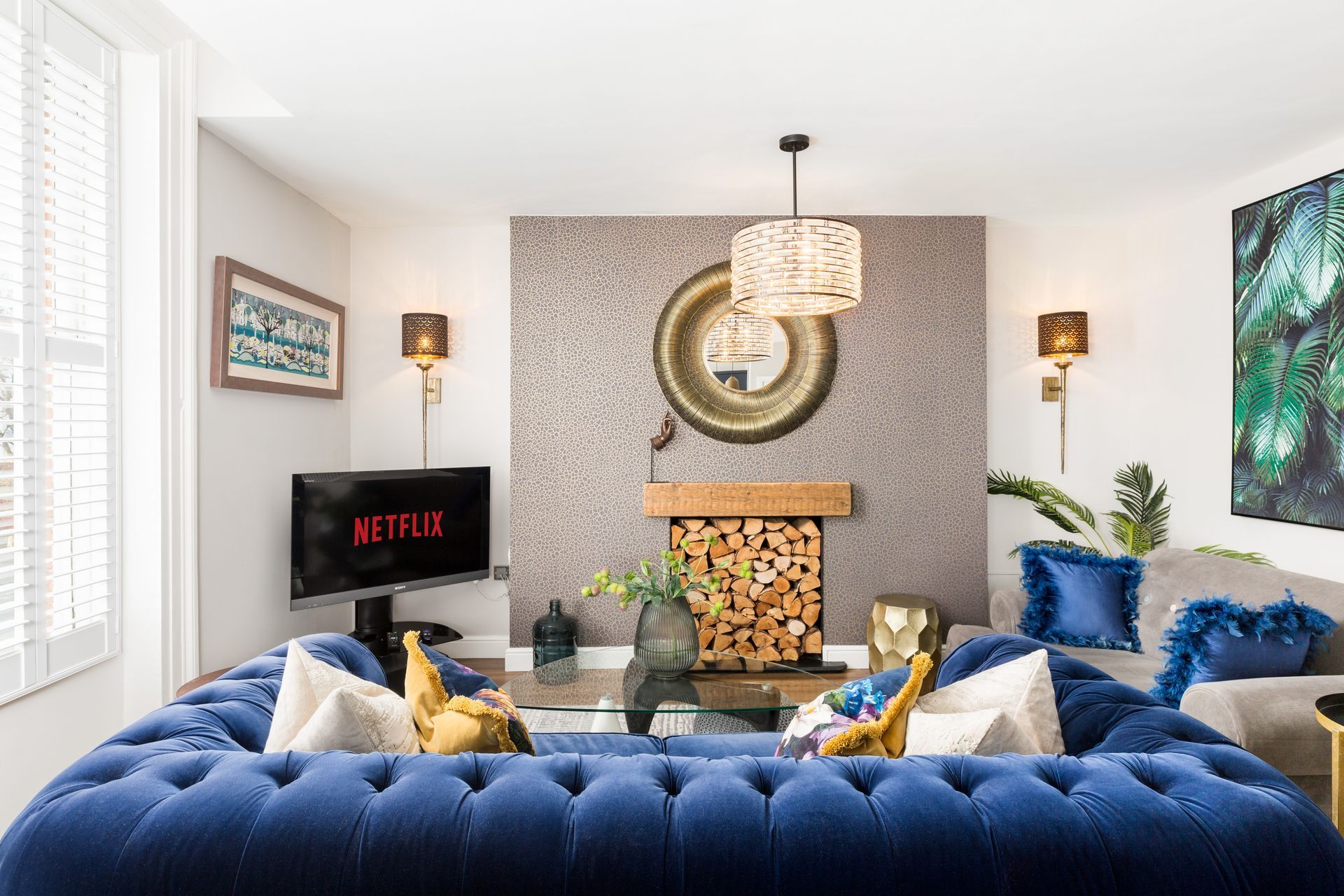 One bedroom apartment with cosy living room with a blue tufted sofa, TV, fireplace, and decorative art.